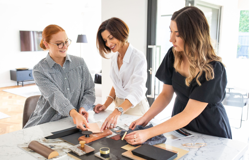 Three women arranging colour, tile and material samples on a table