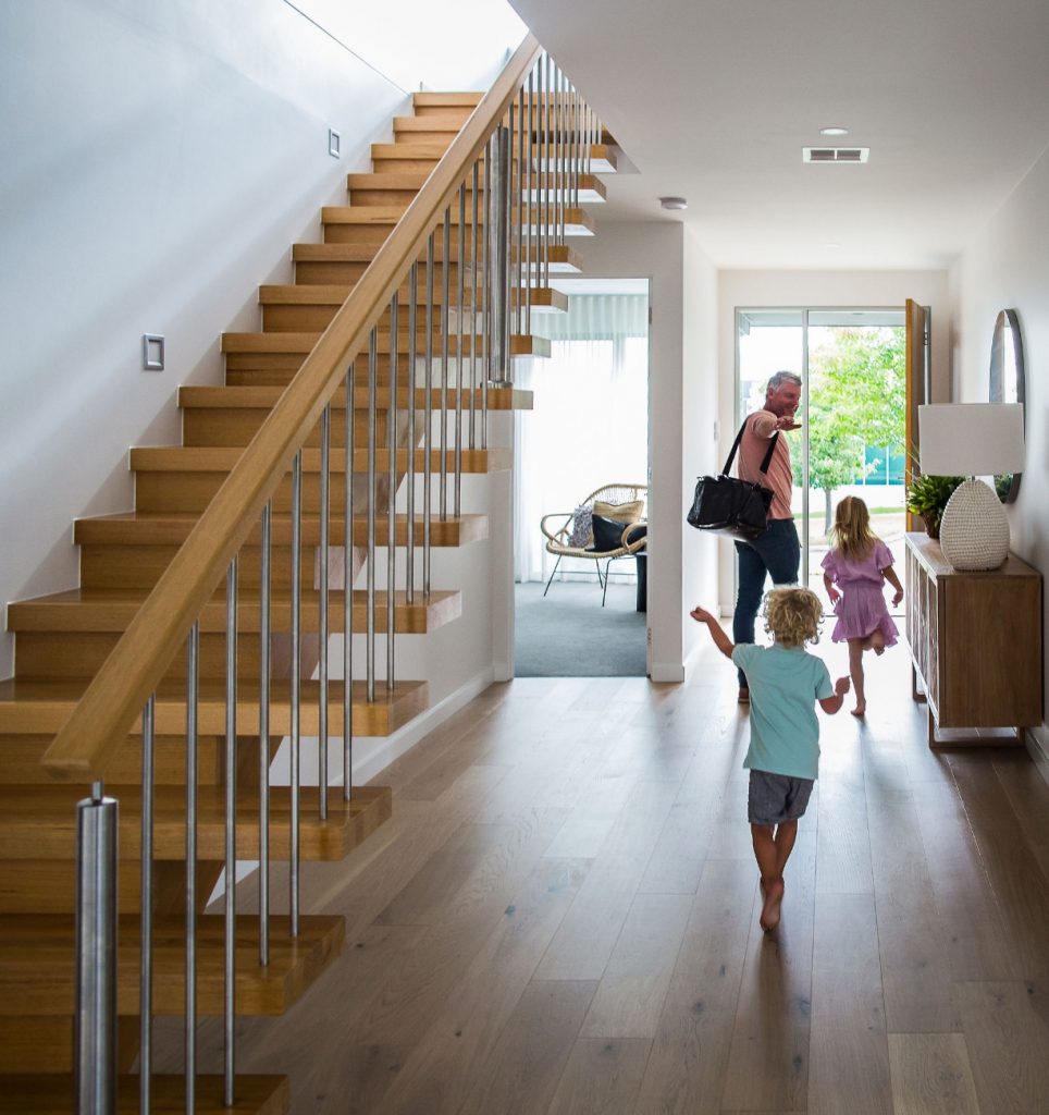 Young family running down a hallway past a timber and steel staircase