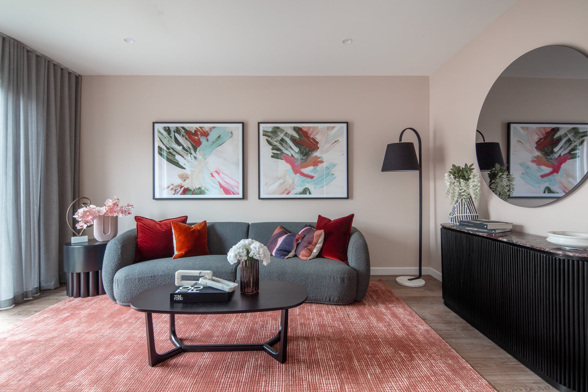 Modern sitting room with grey couch, black coffee table and sideboard, and red and pink soft furnishings