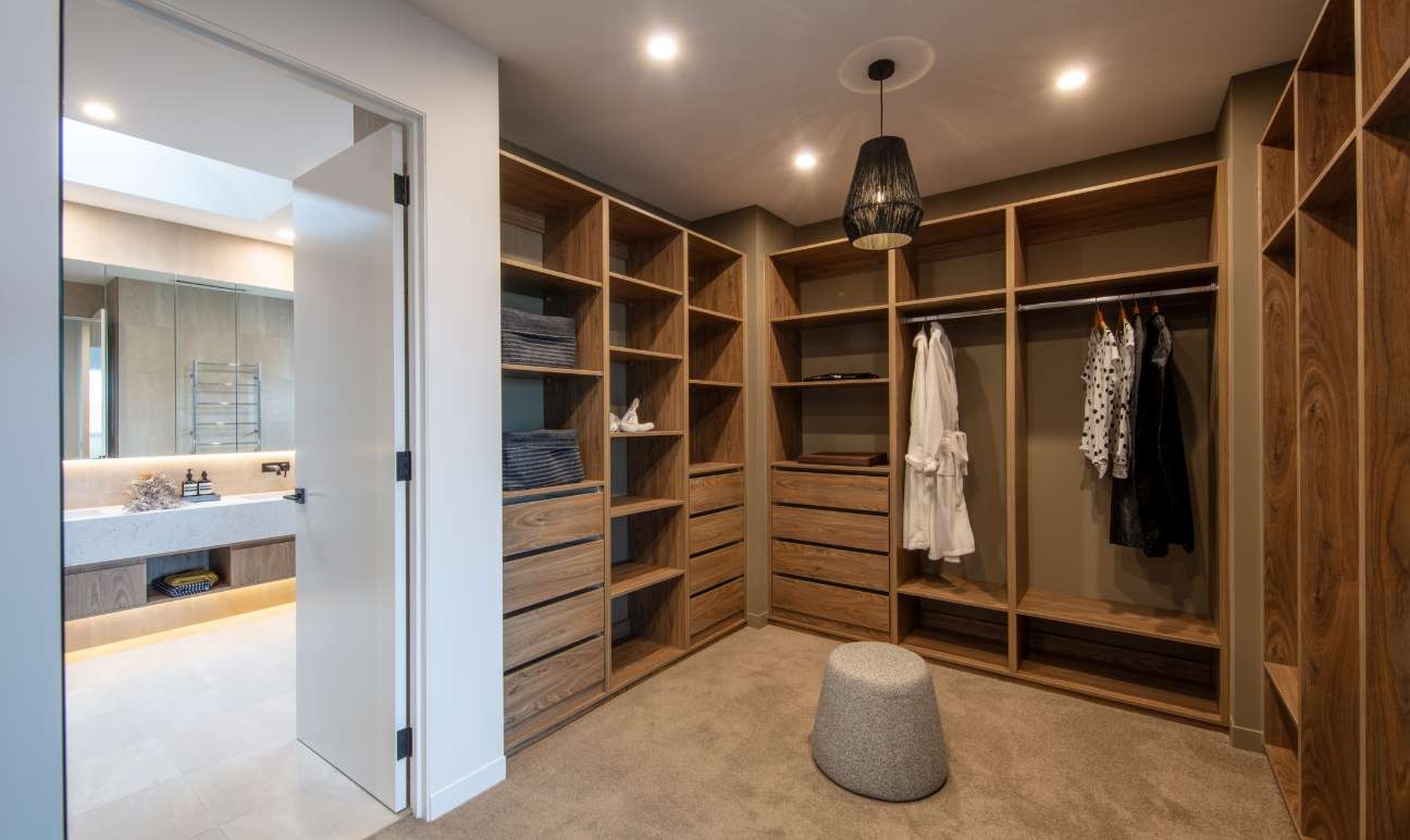 Walk-in wardrobe with open timber cabinetry and warm lighting