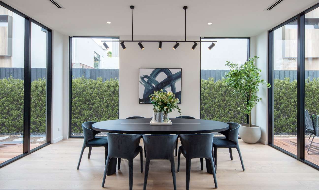 Dining area with dark table and chairs surrounded with floor to ceiling windows and glass sliding doors