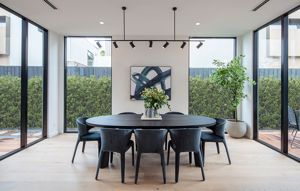 Dining area with dark table and chairs and floor to ceiling windows & glass sliding doors leading to outdoors