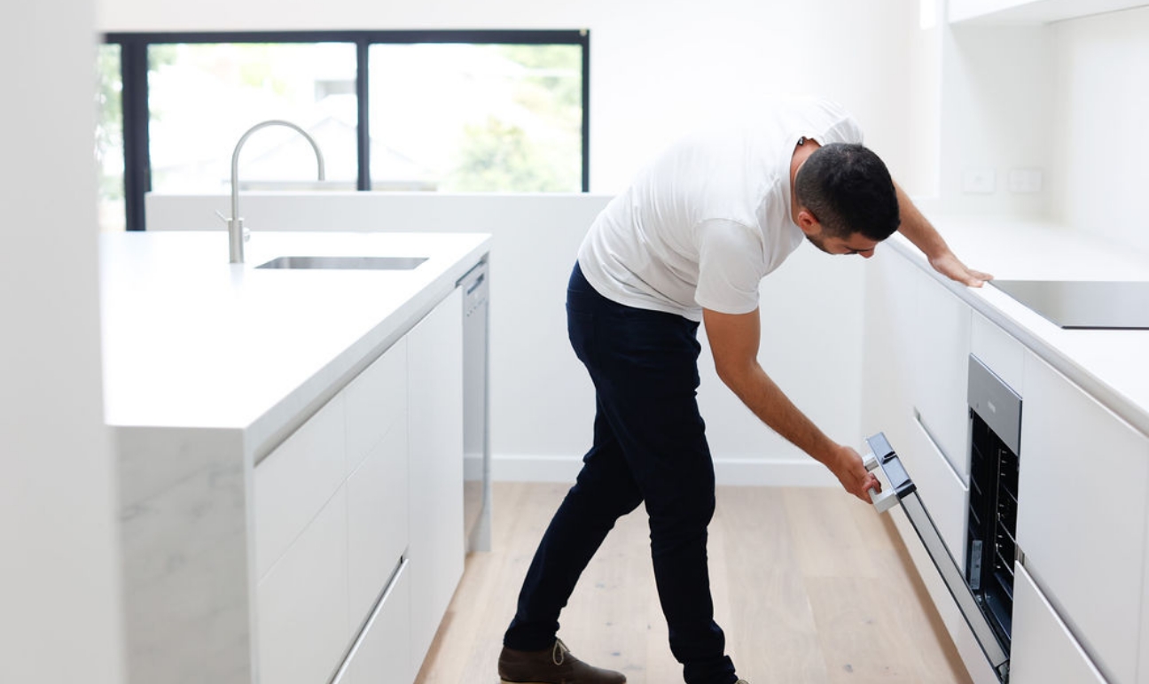 Man opening oven door in modern white kitchen