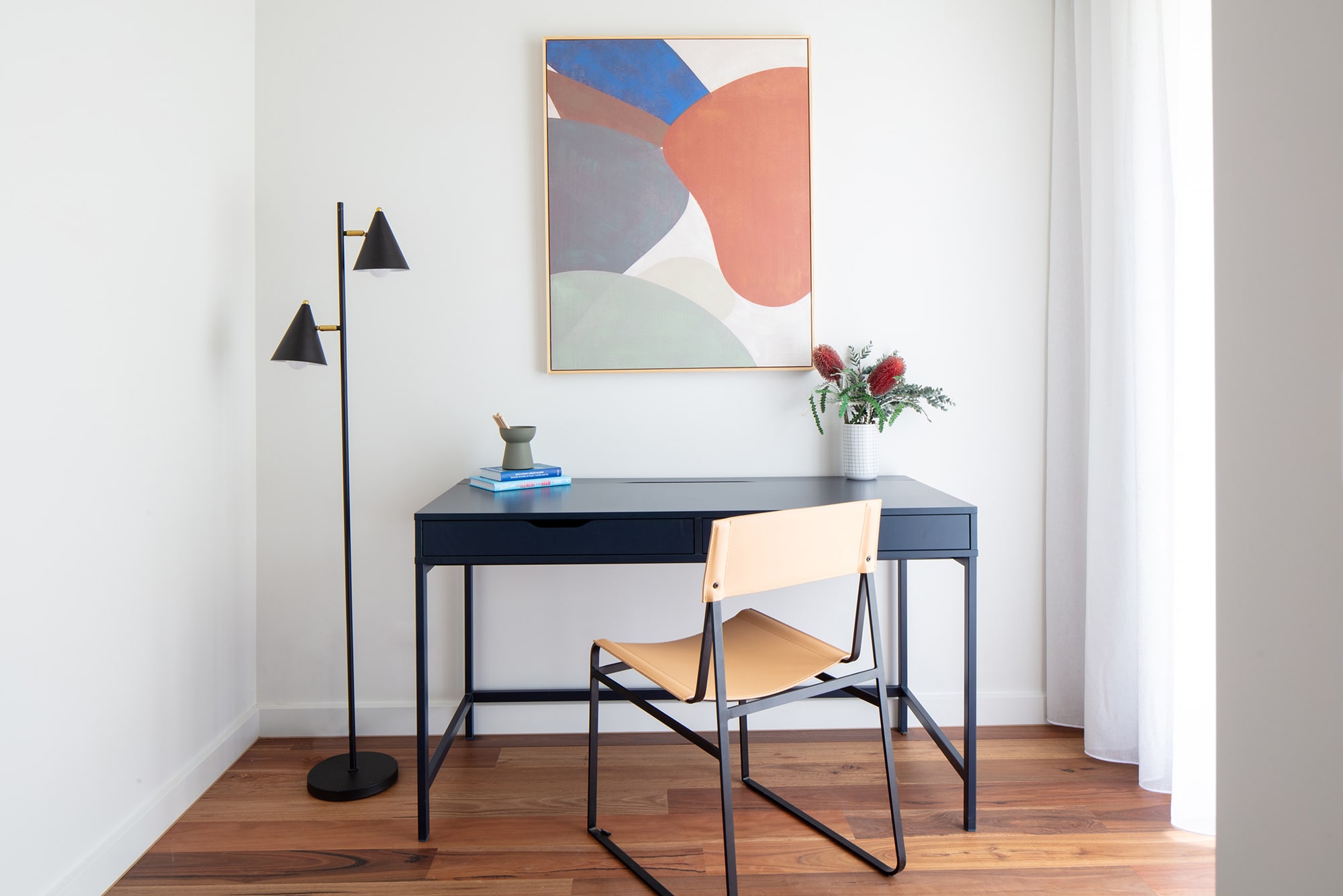 Study nook with desk, chair, floor lamp and modern colourful wall painting