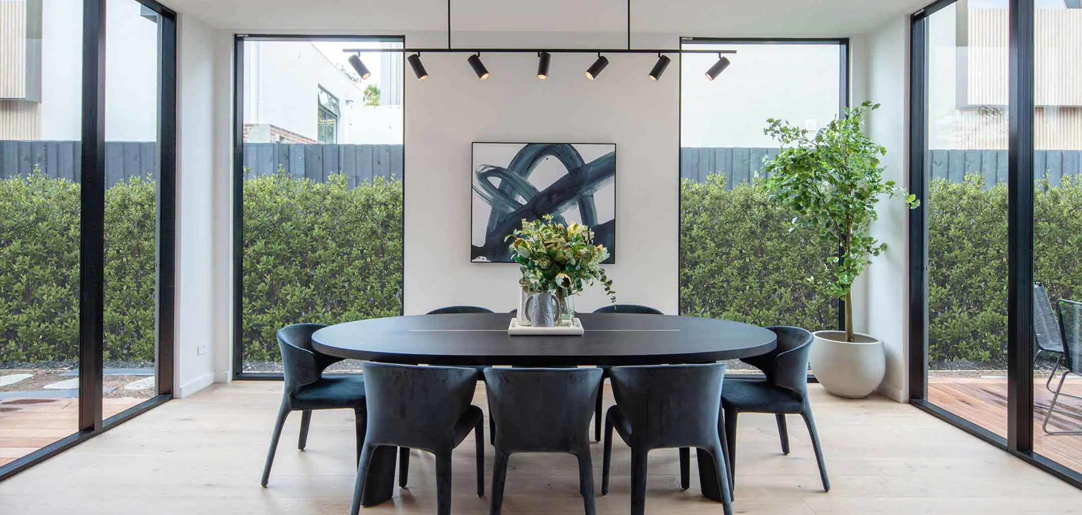 Modern dining room: round black table, eight dark chairs, floral centerpiece, and an abstract painting on a light wall.