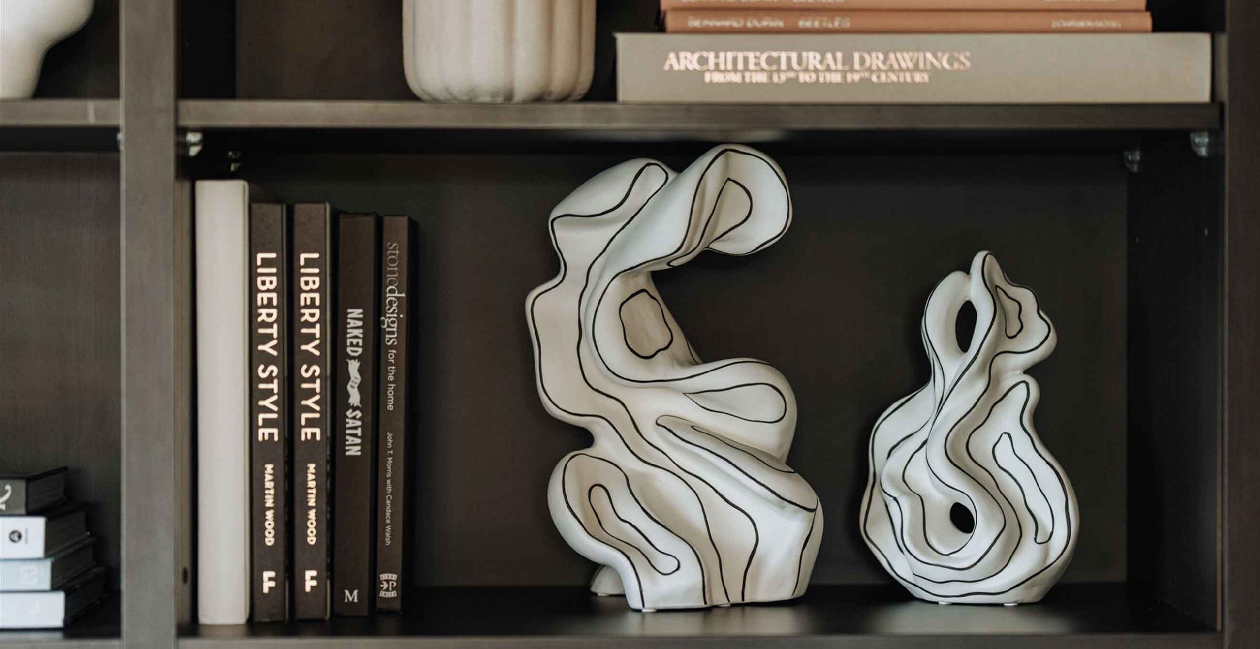 White abstract ceramic sculpture with black outline sits on a shelf beside fashion books.