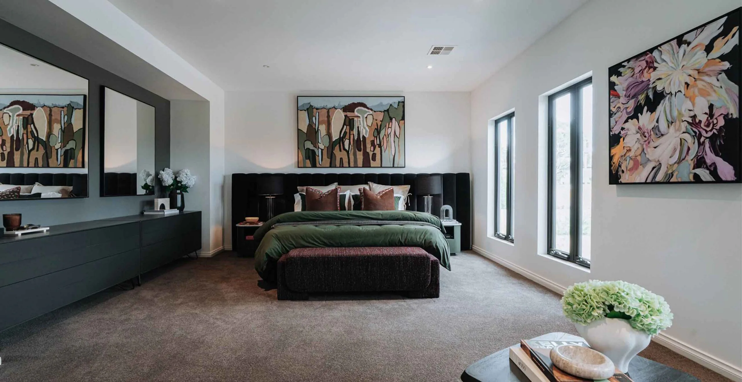 Modern bedroom with a dark upholstered king bed, green bedding, and brown pillows, flanked by nightstands and lamps.