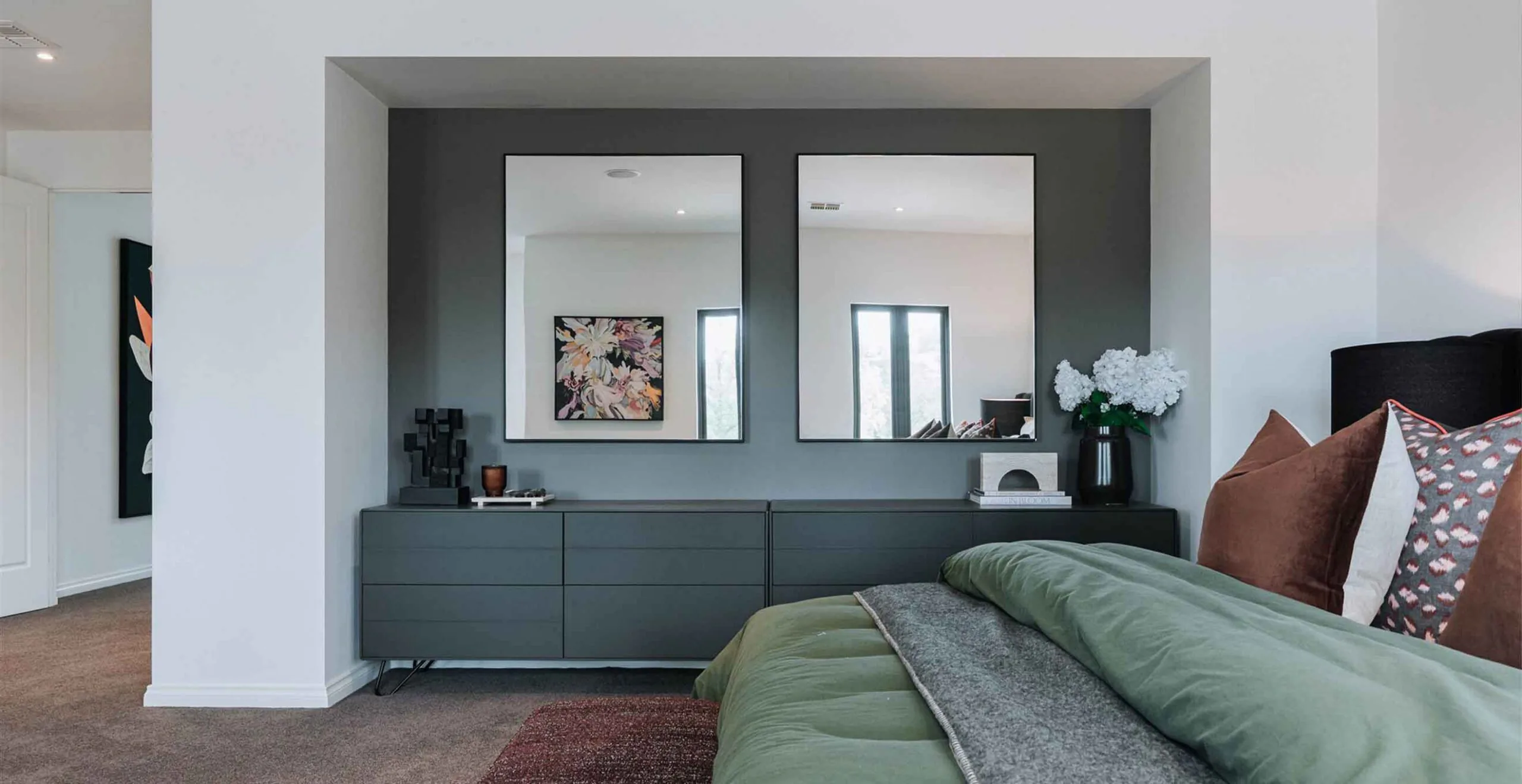 Modern bedroom interior with a dark gray accent wall, two framed mirrors above a sleek dresser, and decorative items on top.