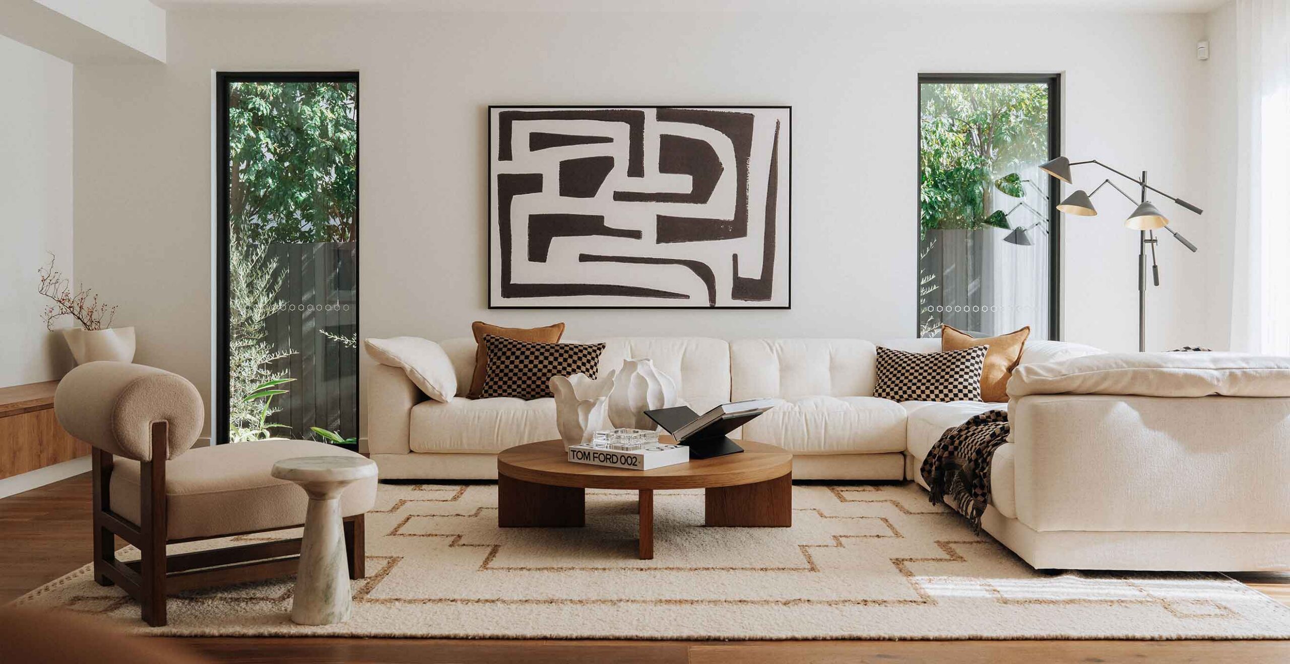 Bright modern living room with a white sectional, black-and-white abstract painting, two tall windows, and a multi-arm floor lamp.