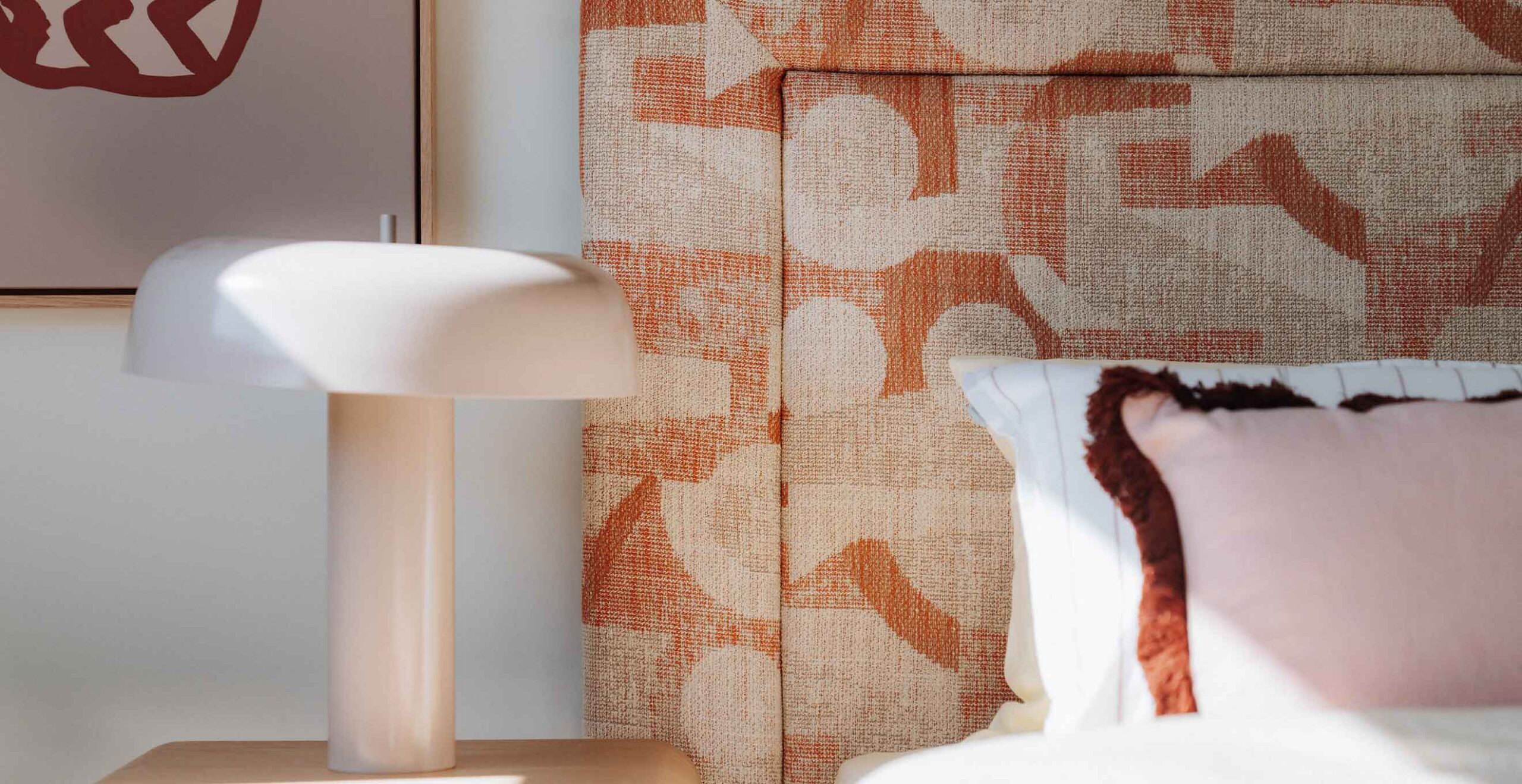 White bedside lamp on a light wood nightstand beside a patterned orange couch and a pale pink pillow.