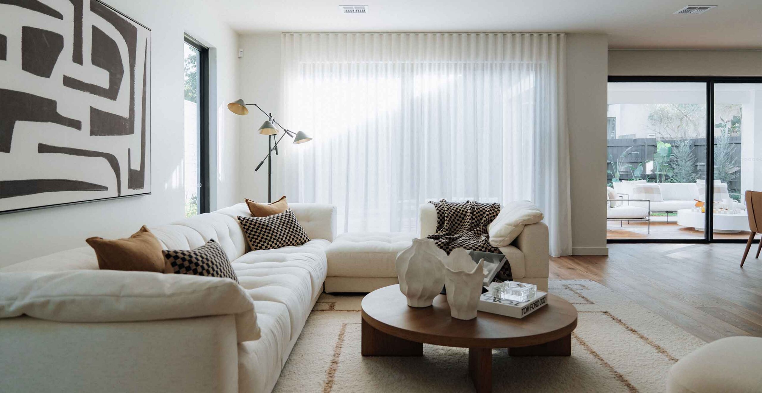 Modern living room with white sectional sofa, checkered pillows, and a multi-arm floor lamp against sheer white curtains.