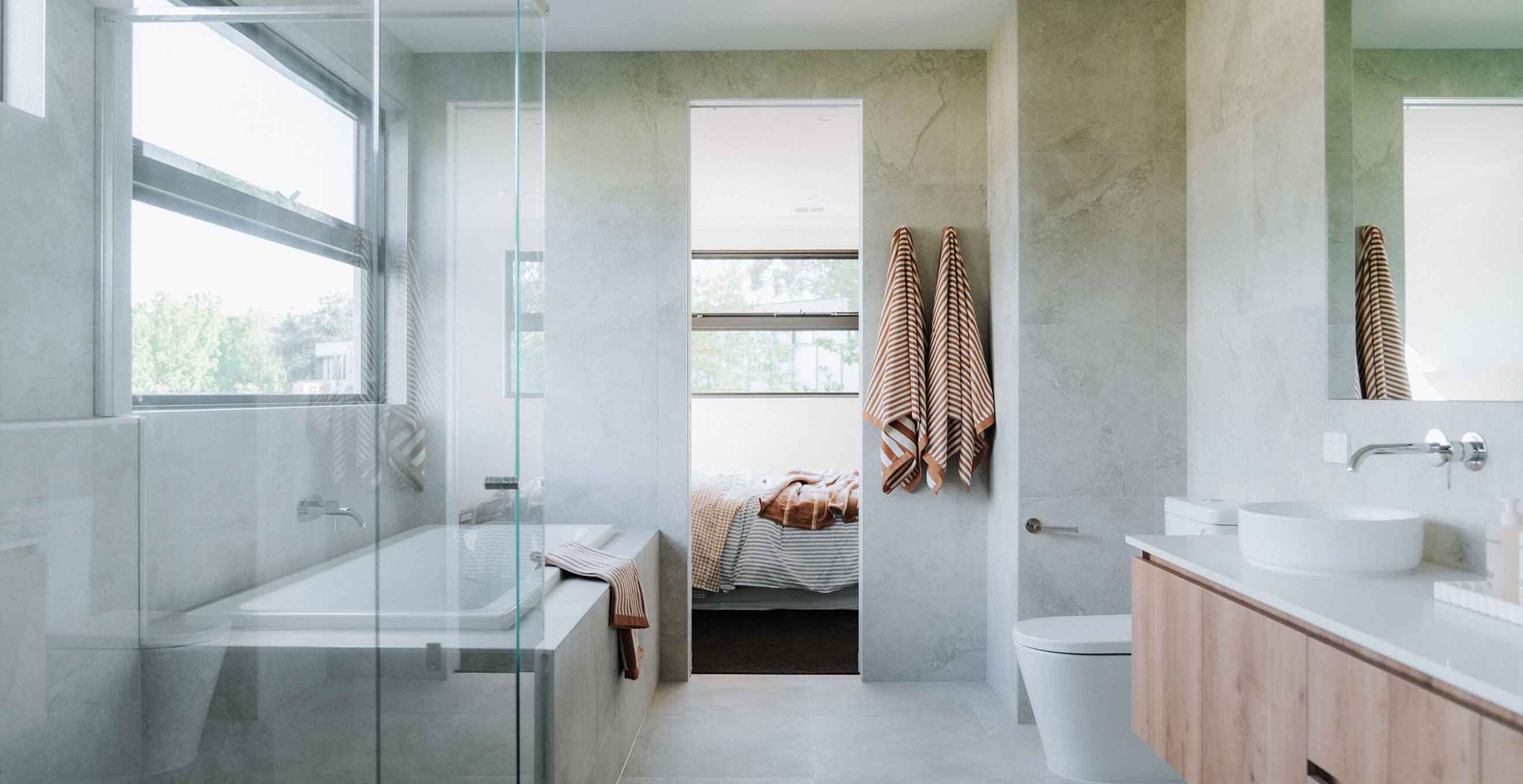 Bright modern bathroom featuring a glass shower, bathtub, and orange striped towels on the wall by the doorway.