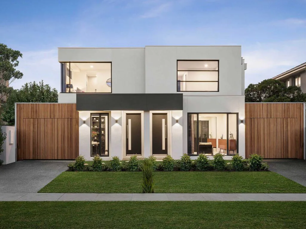 Modern two-story house with white exterior, black entry doors, and large glass windows; wooden privacy fencing and a green lawn.