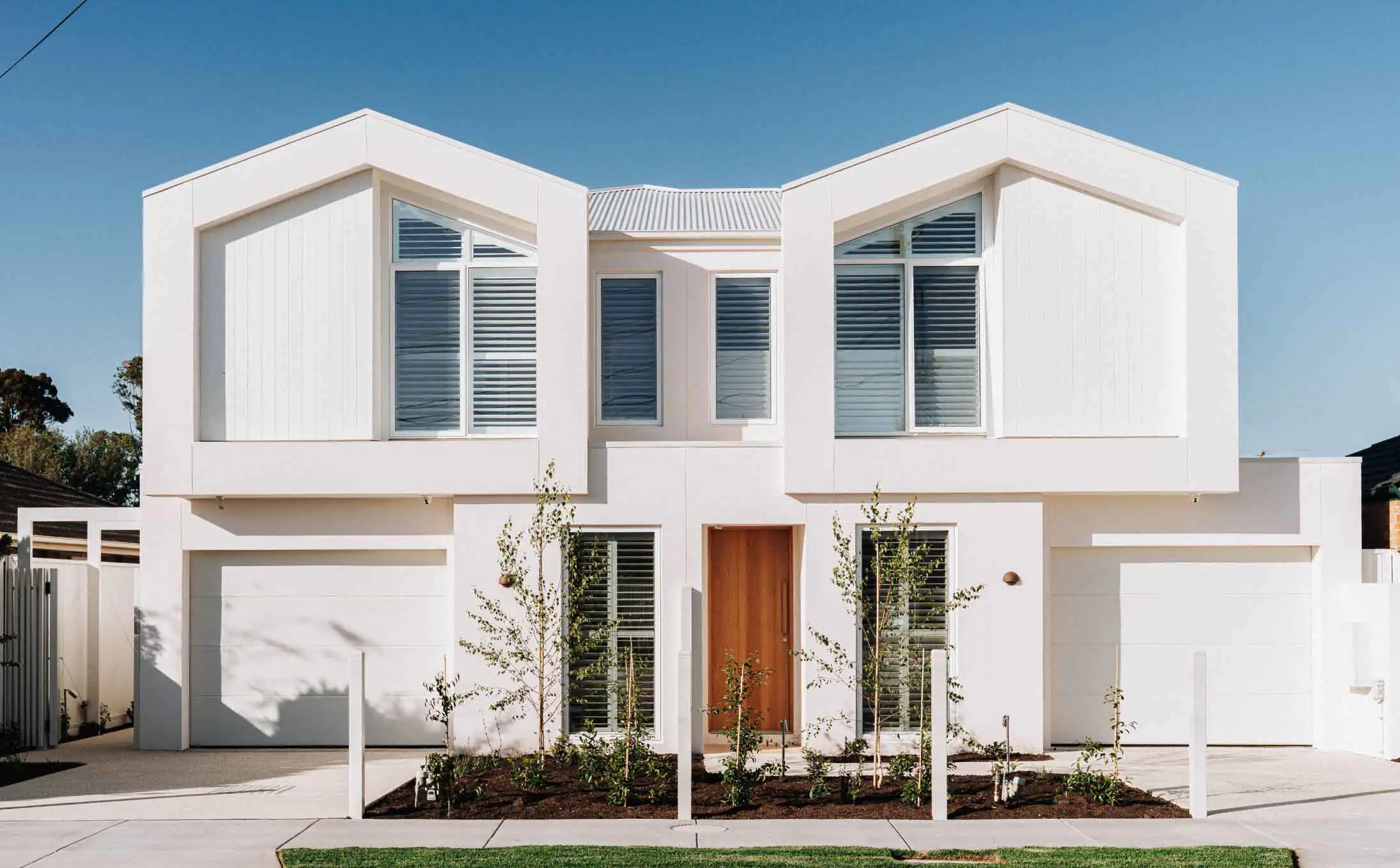 Modern white two-story house with large, angular windows and a wooden front door under a clear blue sky.