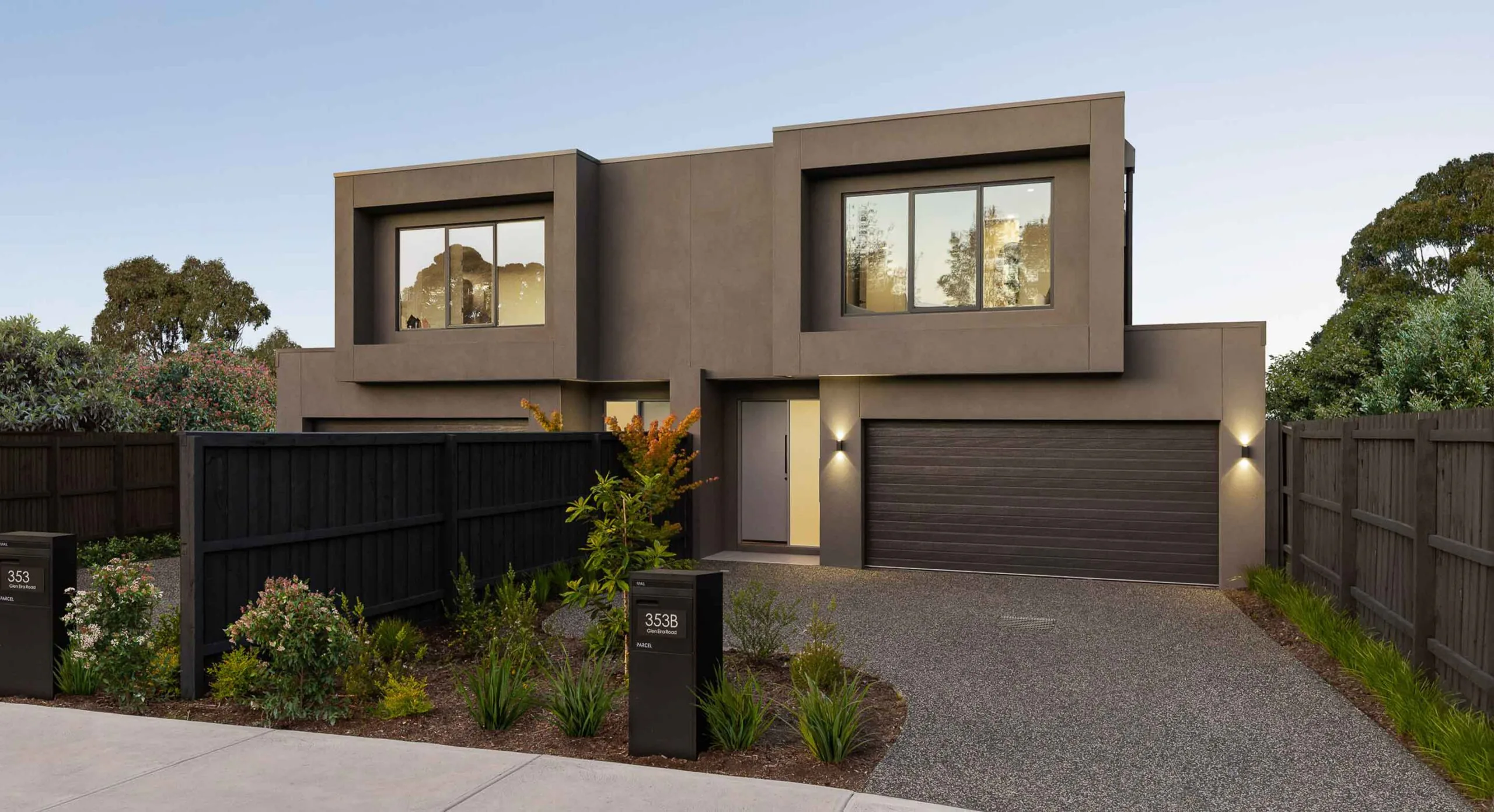 Modern two-story brown residence with a two-car garage and tall privacy fence in a landscaped front yard