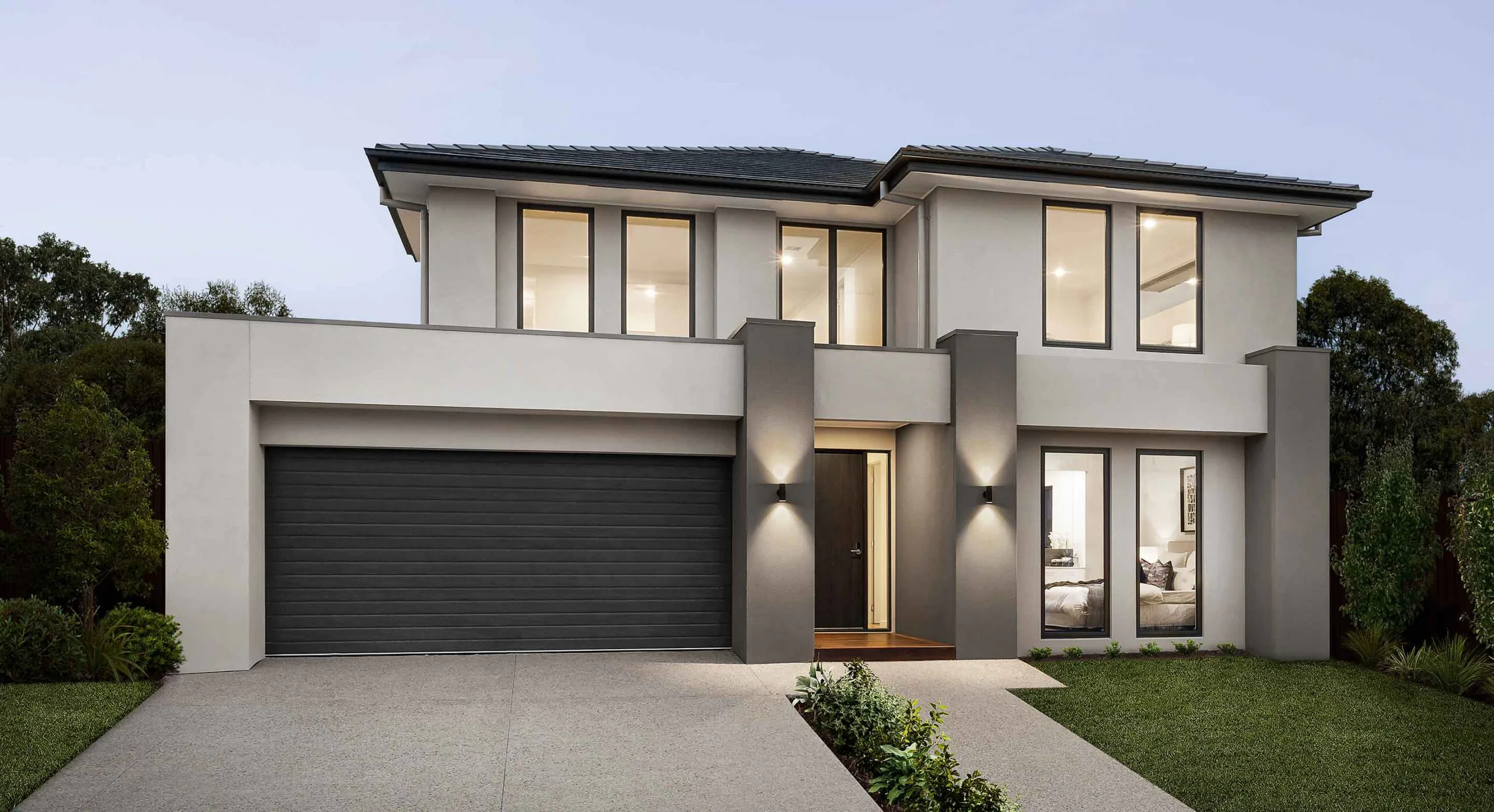 Modern two-story house with a wide gray facade, large front windows, and a dark garage door; landscaped yard and driveway.