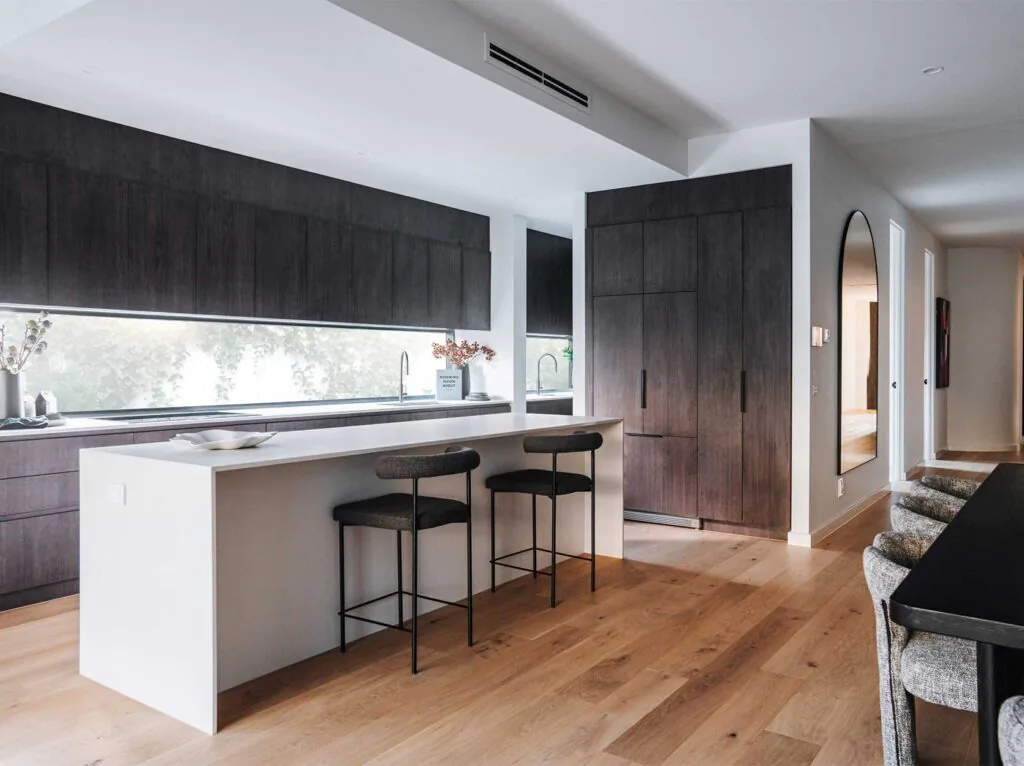 Open-concept kitchen with a white island, dark wood cabinets, and three black bar stools.