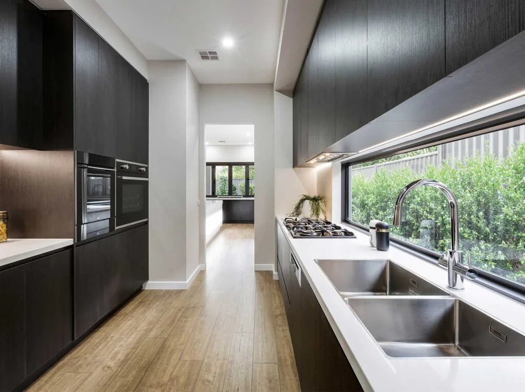 Modern kitchen with dark wood cabinets, white countertops, gas cooktop, and a large window over the sink.