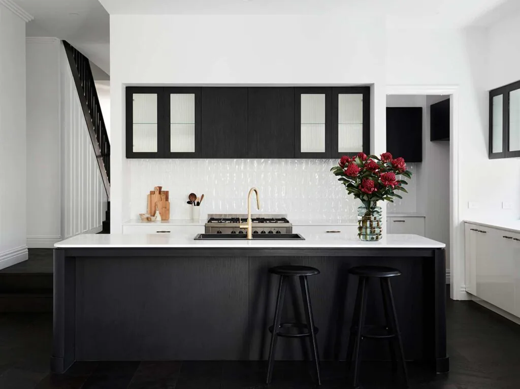 Modern kitchen with a dark island, gold faucet, and a red bouquet on the white countertop against black upper cabinets.
