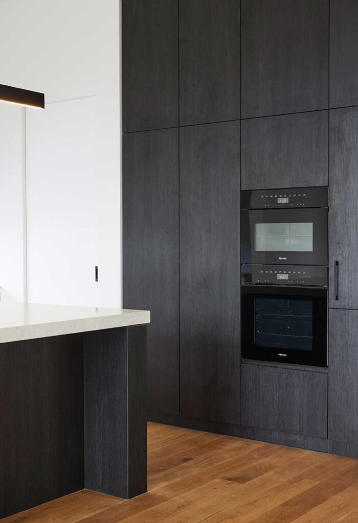 Kitchen with dark wood cabinets and built-in double oven unit, white countertop island, and warm wooden flooring.