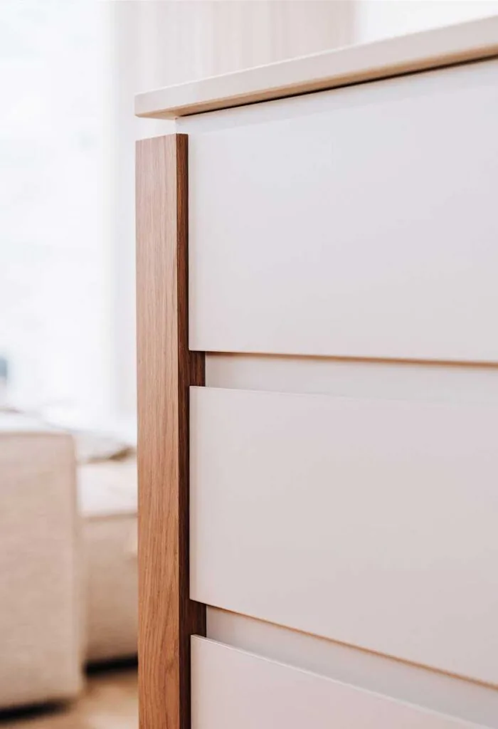 Close-up of a modern dresser with white drawer fronts and natural wood side trim.