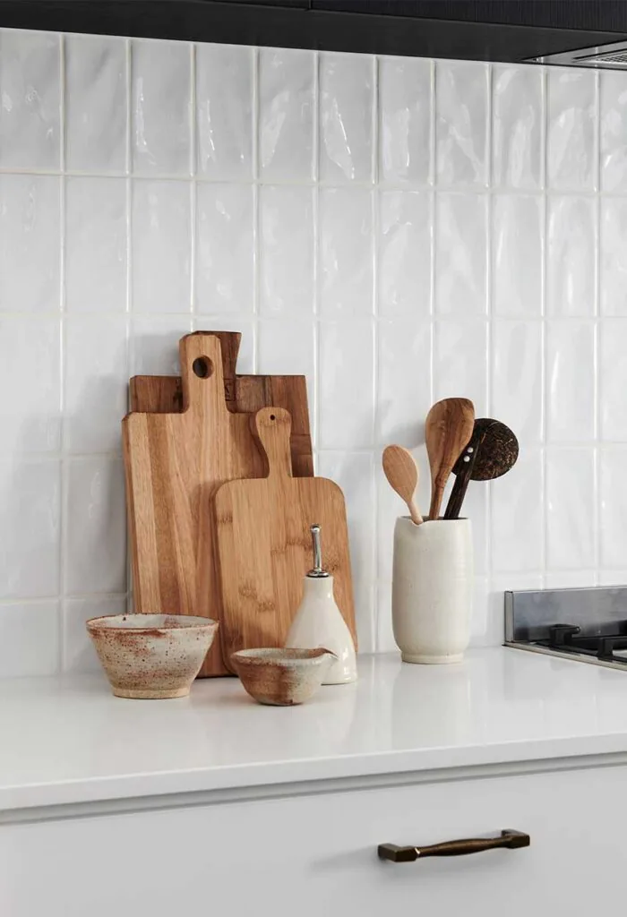 White kitchen counter with wooden cutting boards, ceramic bowls, and a utensil holder near a stovetop.