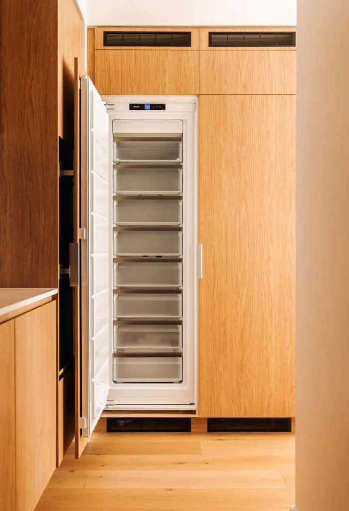 Open tall freezer in a modern wood kitchen with multiple clear drawers and the door swung outward (empty freezer).