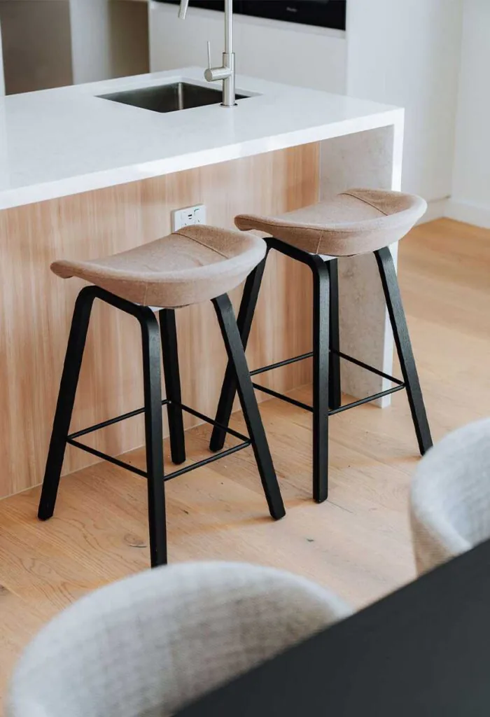 Modern kitchen island with a white countertop and two beige upholstered bar stools with black metal legs.