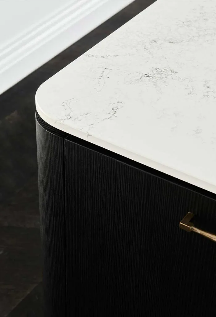 Close-up of a white marble countertop with a rounded edge atop a dark wood cabinet with a brass handle.