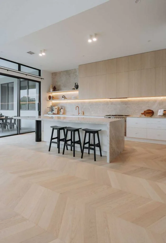 Modern kitchen with a marble island, three black stools, light wood cabinets, and large glass doors to the patio.