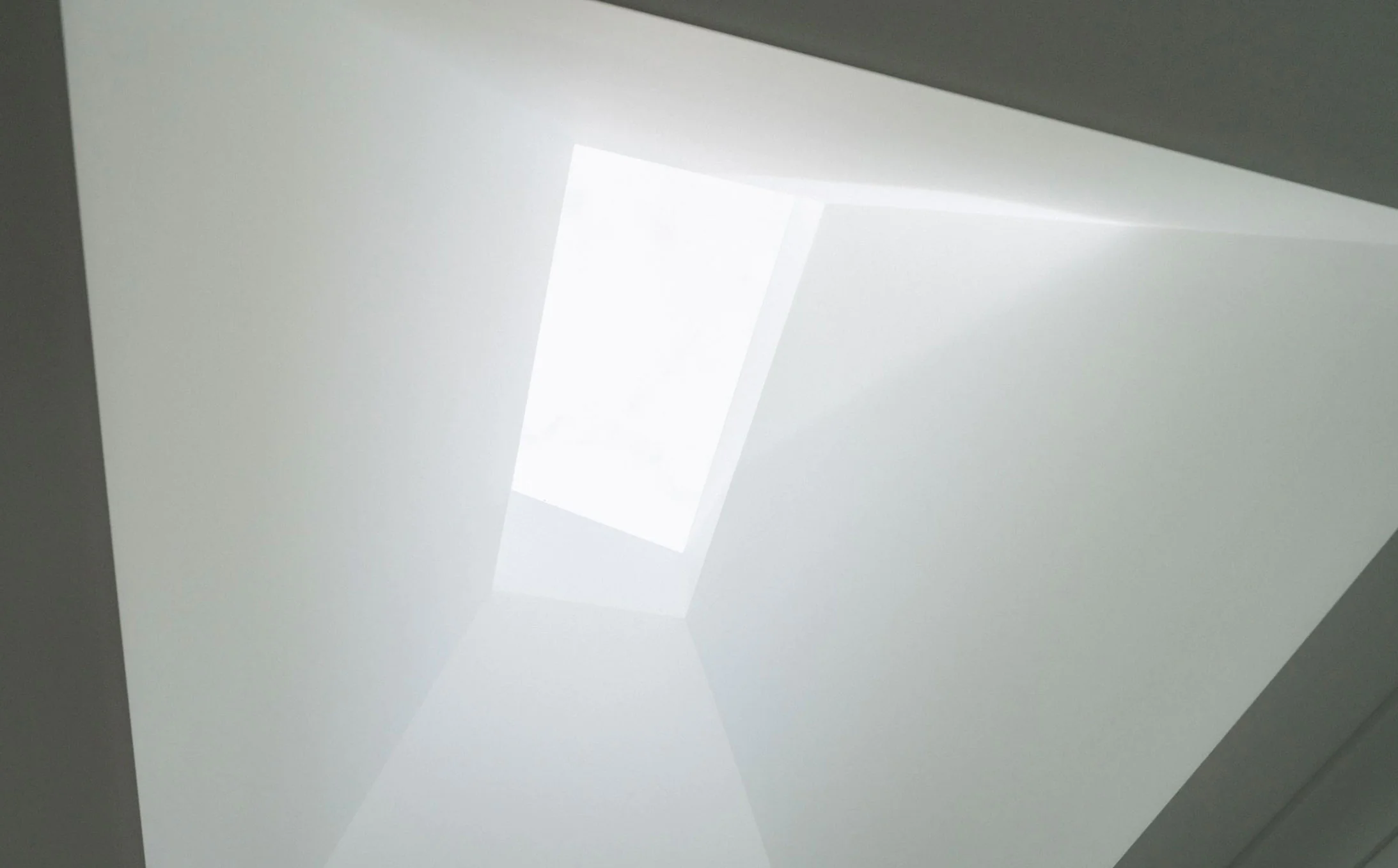 Abstract interior ceiling with overlapping white panels and diagonal light reflections on a gray surface, creating geometric shapes.