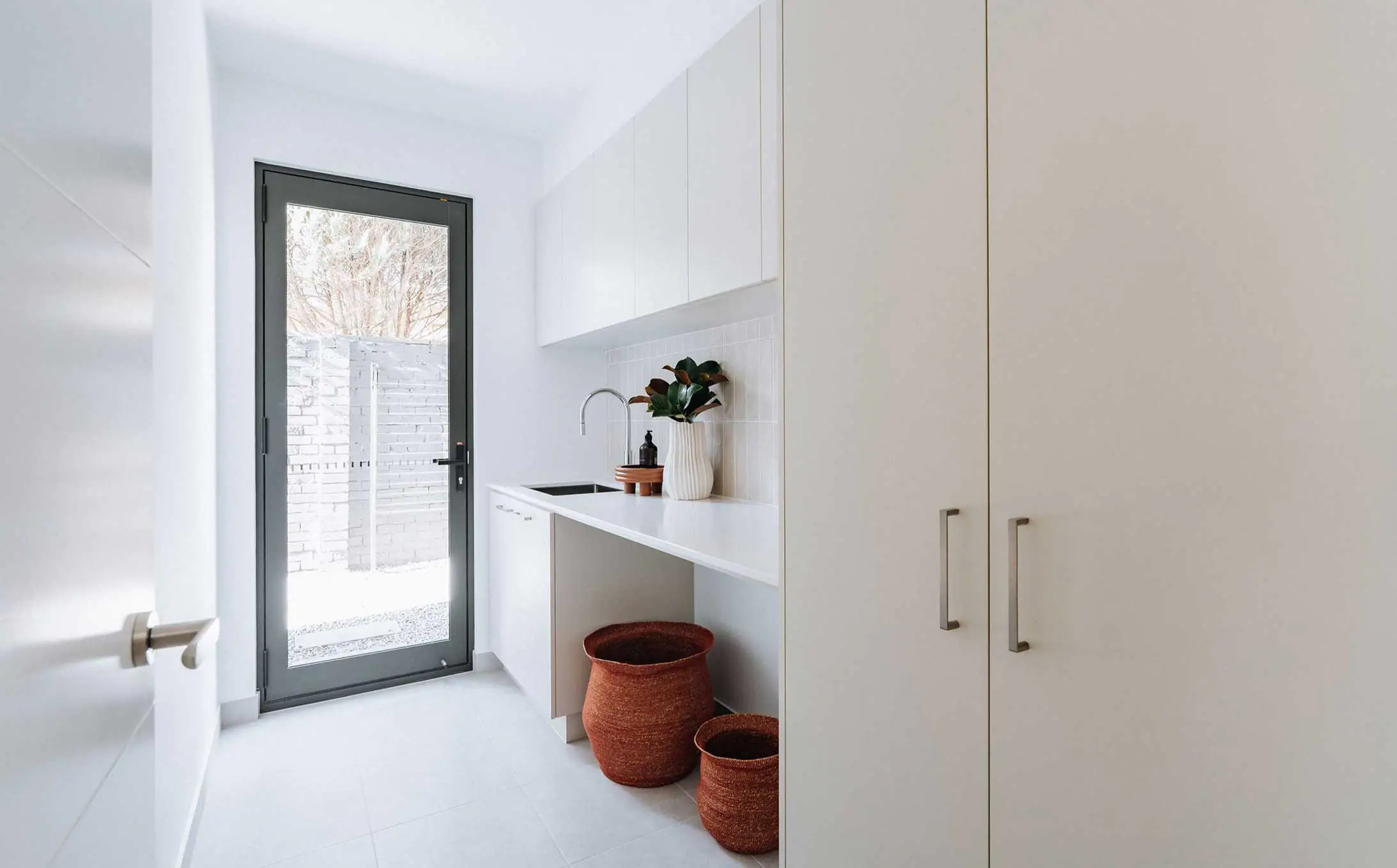 Bright, modern kitchen with white cabinetry, a sink, and brown wicker baskets by the counter