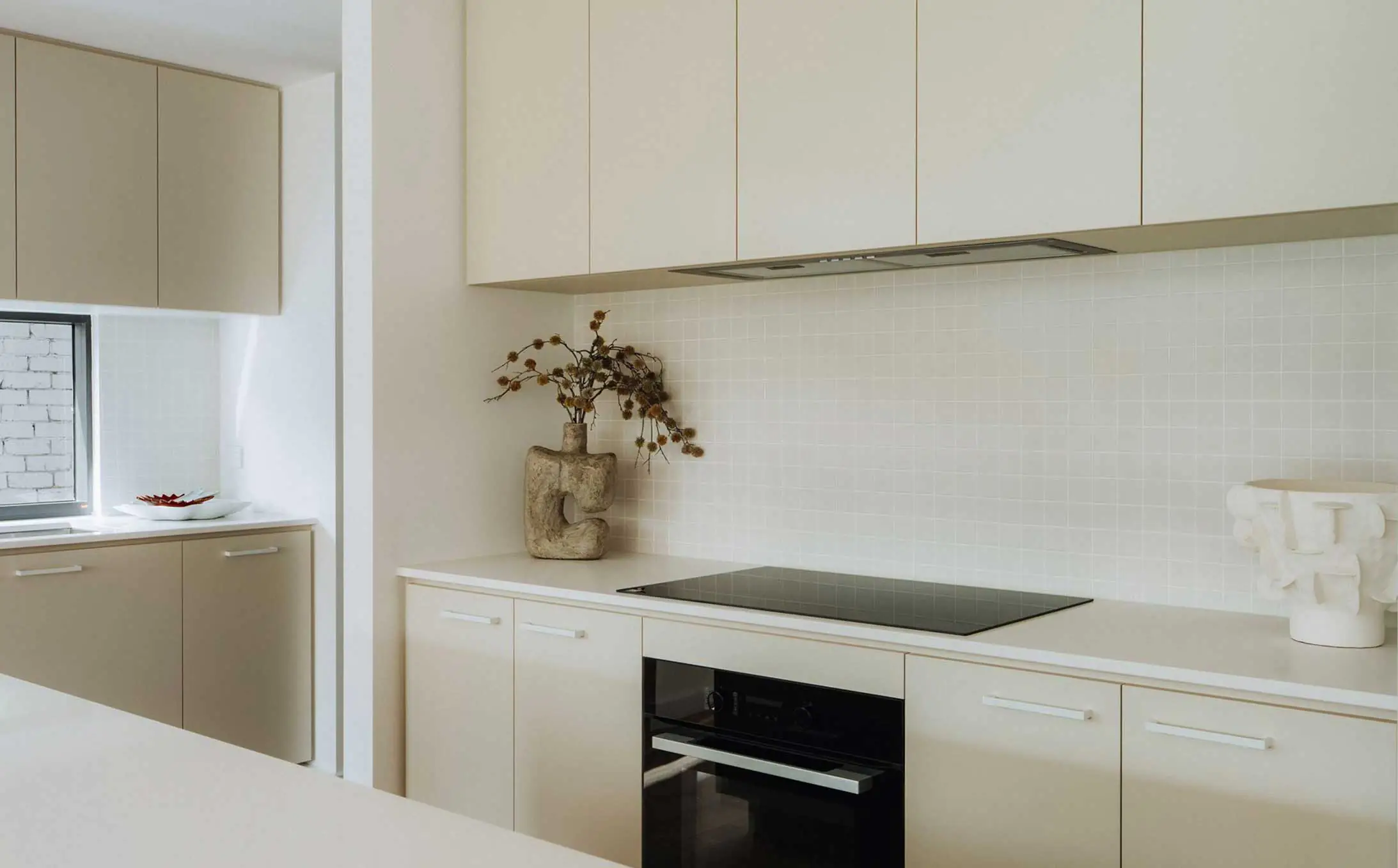 Modern beige kitchen with tall upper cabinets, a white tiled backsplash, and a built-in oven.