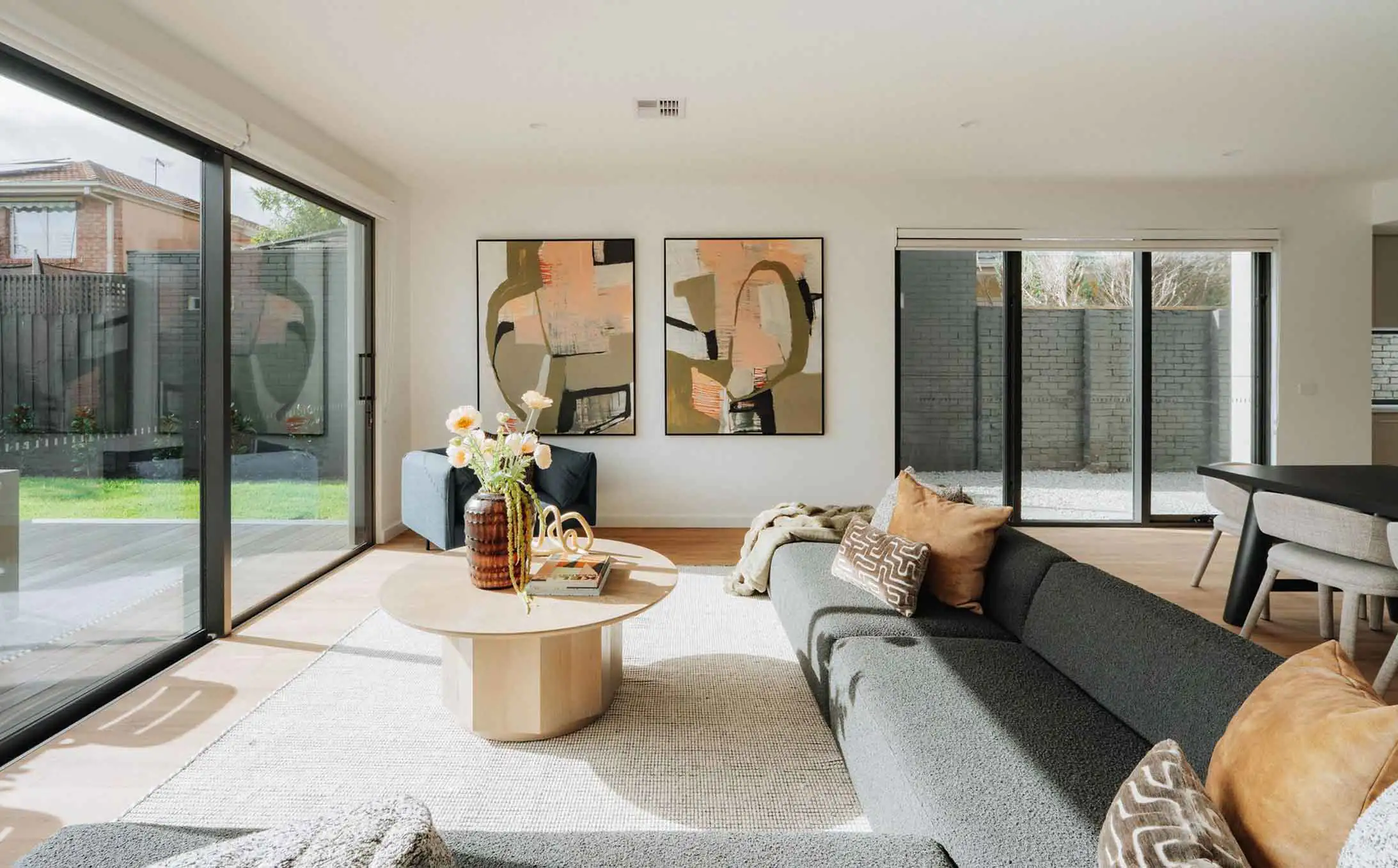 Bright living room with glass sliding doors to a fenced backyard, abstract wall art, and a gray sectional sofa with brown pillows.