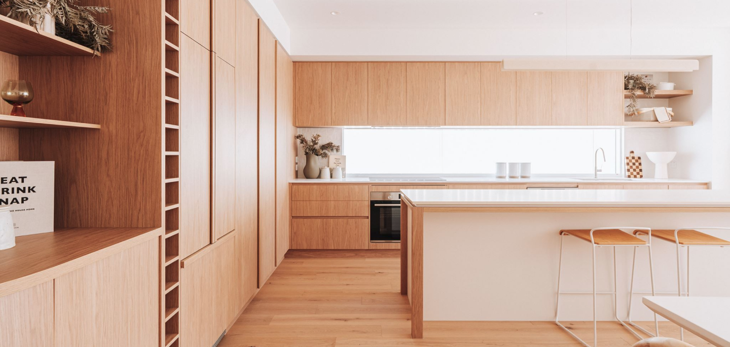 Bright minimalist kitchen with full-height wooden cabinets, a central island, and light wood flooring. Bar stools line the island edge.