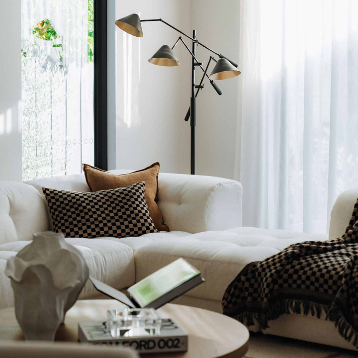 Bright living room with a white sectional, brown checkered pillows, a modern multi-arm floor lamp, and a round coffee table.