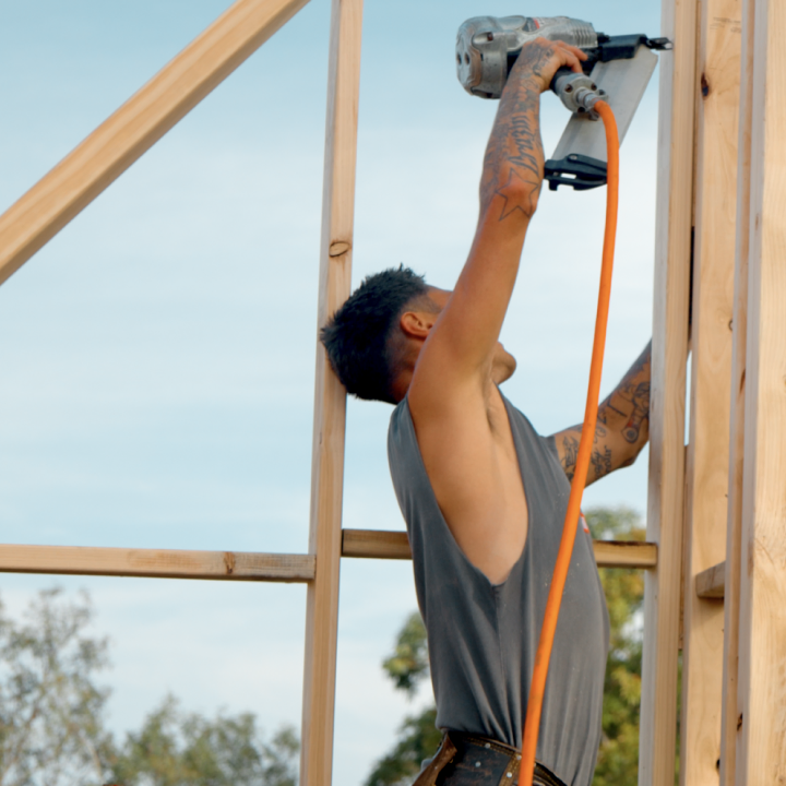 Construction worker using a power saw to cut a wooden beam in a framed building.