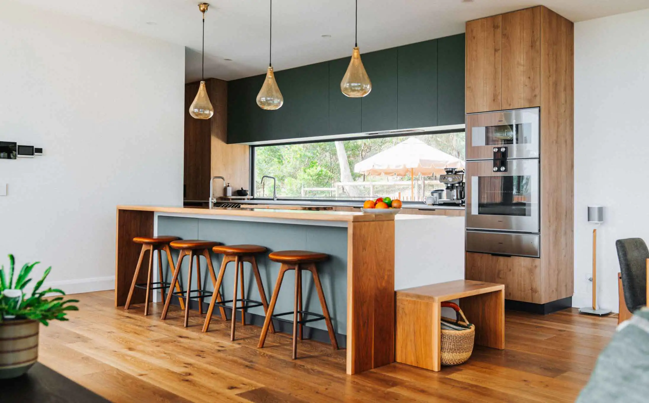Open-concept kitchen with a wooden island, grey bar, and four wooden stools facing a large window.