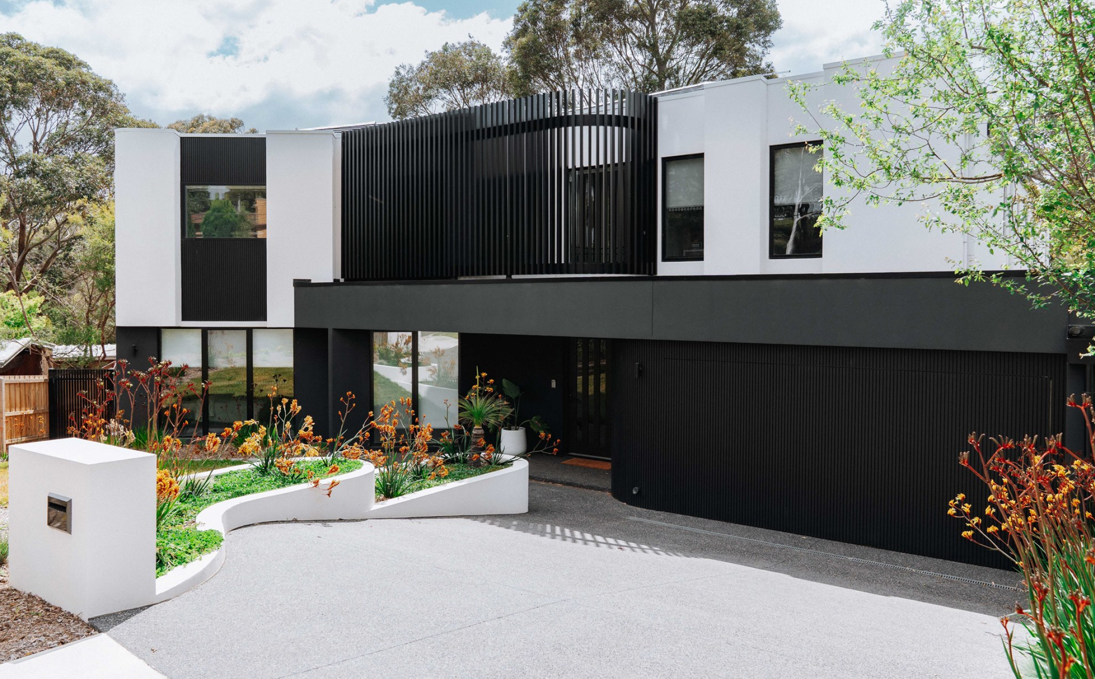 Modern two-story house with white walls, black vertical louver screen, and landscaped front yard.