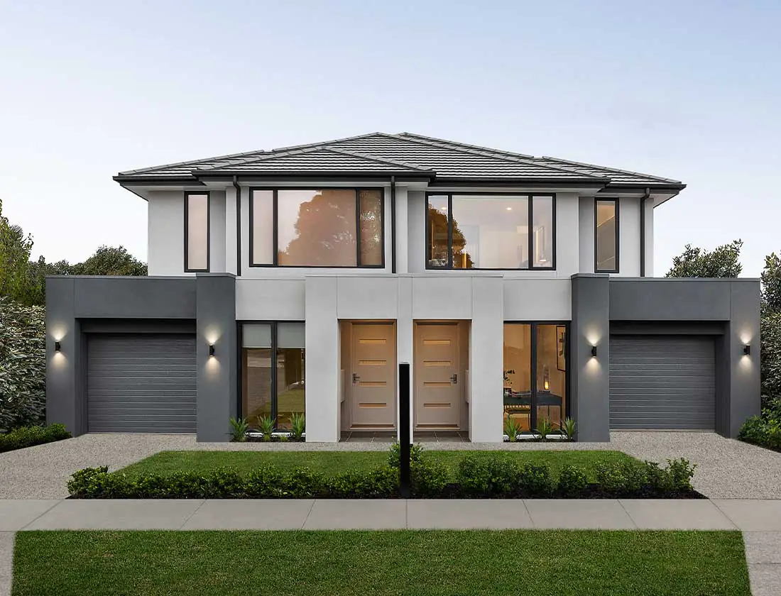 Two-story modern house with two front doors, twin garages, and a manicured front yard with hedges and a sidewalk.