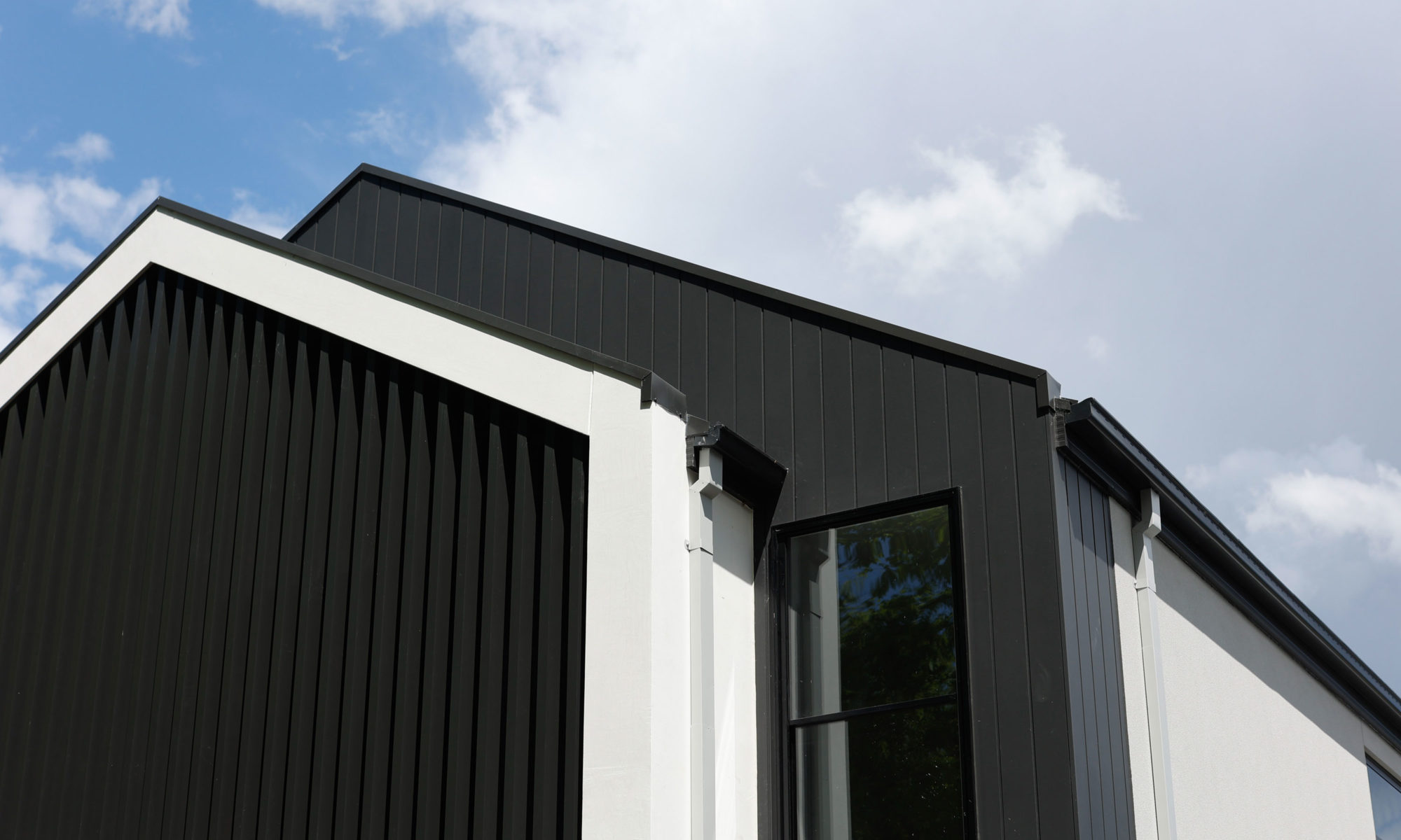 Black & white exterior against blue sky|||Modern kitchen with white cabinetry and stone island|Bright living area with large glass sliding doors to a backyard|Man opening oven door in modern white kitchen|Black & white exterior against blue sky with clouds||