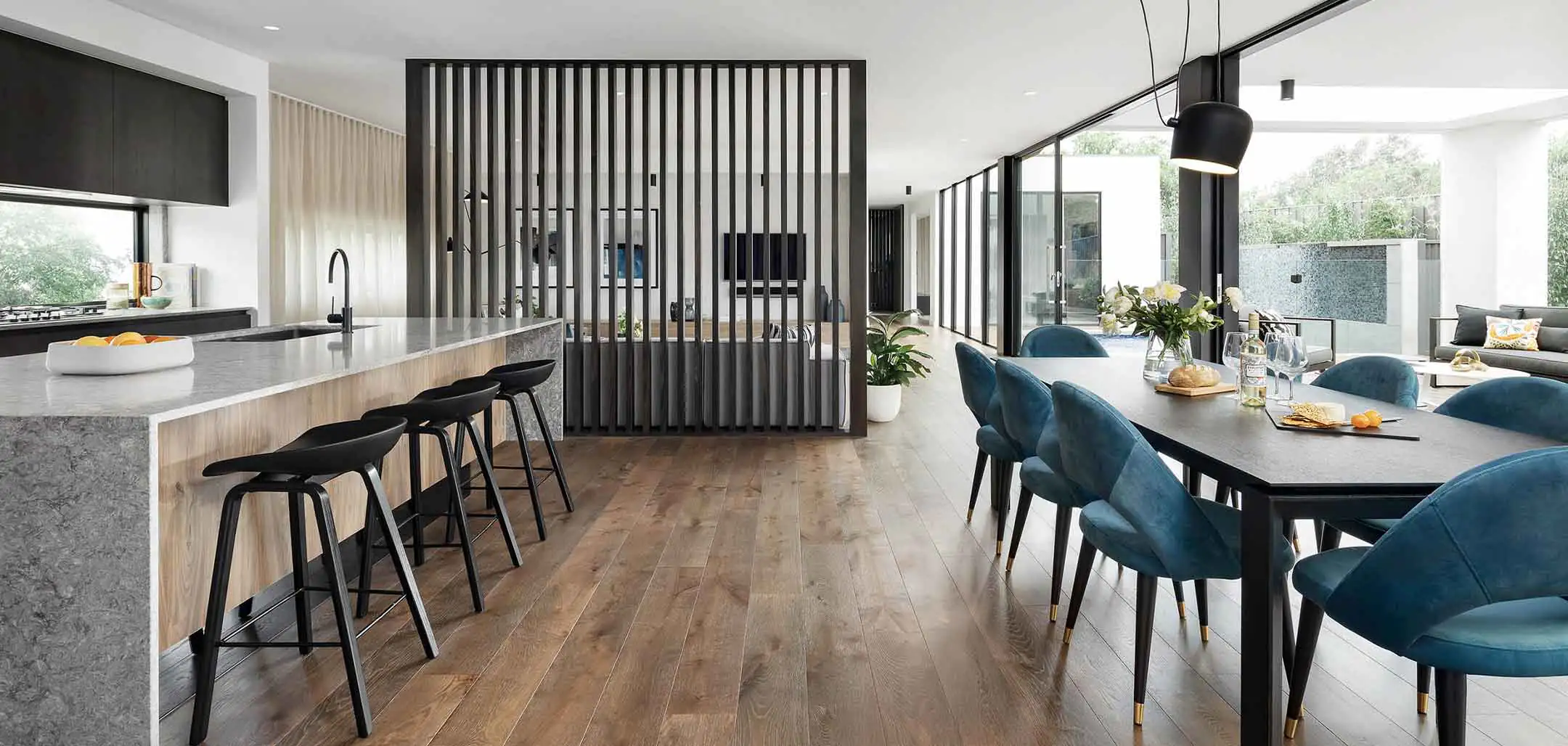 Open-concept kitchen and dining area with a marble island, black bar stools, and blue upholstered dining chairs