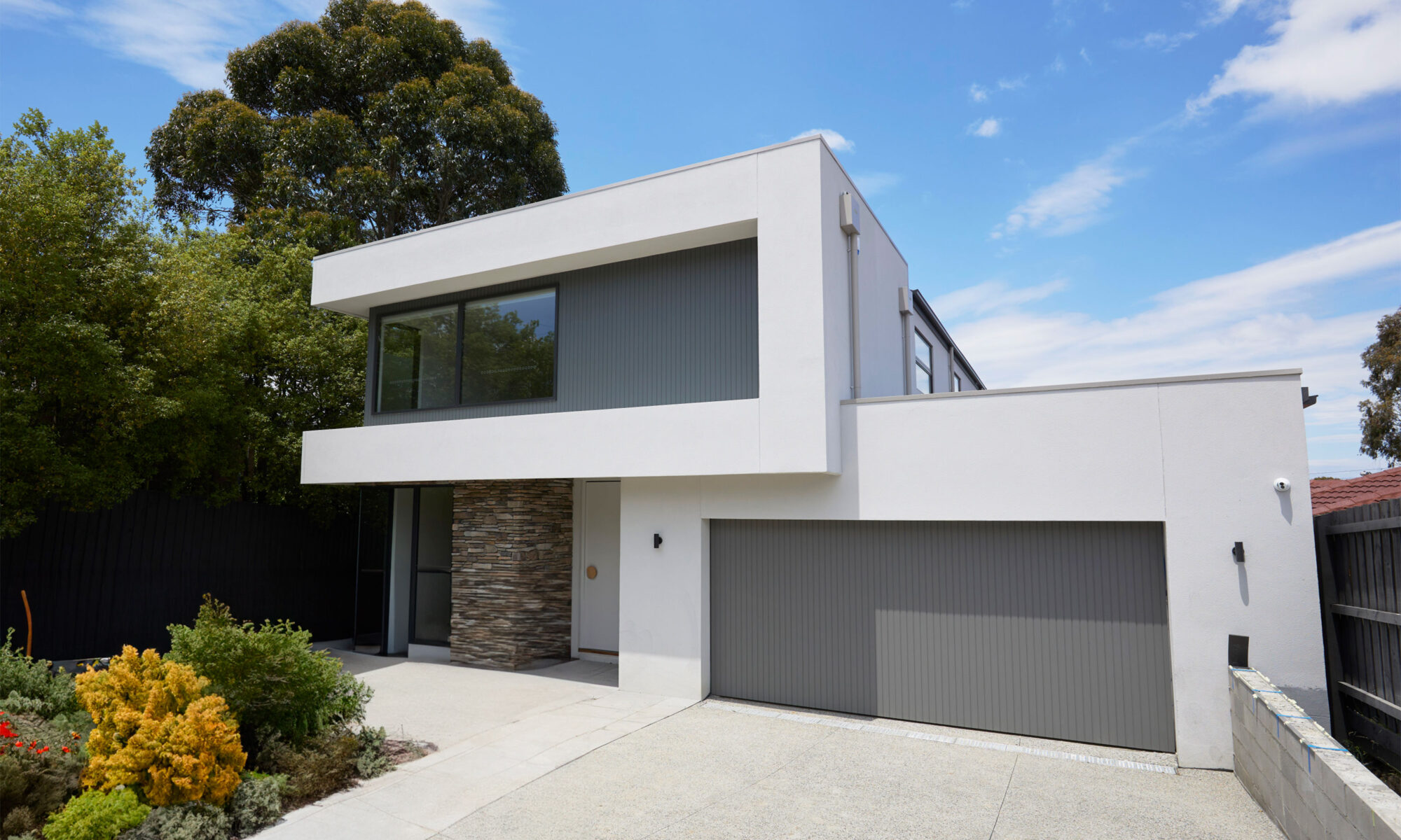 Double storey facade in white & grey||||Double storey facade against blue sky with clouds|Modern bathroom with large white bath tub against vertical tiled wall|Bright entry hallway and timber staircase leading to second storey|Custom black kitchen cabinetry and stone bench top|Double bathroom vanity with stone bench tops|Double storey facade in white & grey