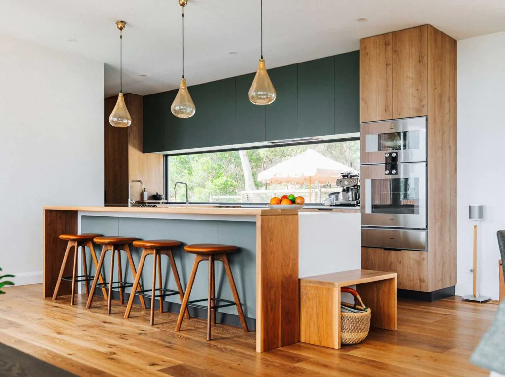 Modern kitchen with a wooden island, four wooden bar stools, dark green upper cabinets, and a built-in stainless steel oven unit.