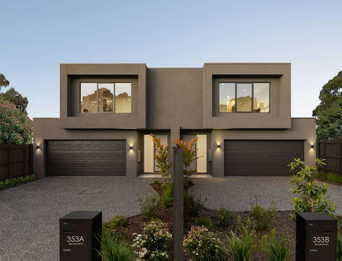 Modern two‑story duplex with dark grey facade, two garage doors, and a small landscaped front yard.