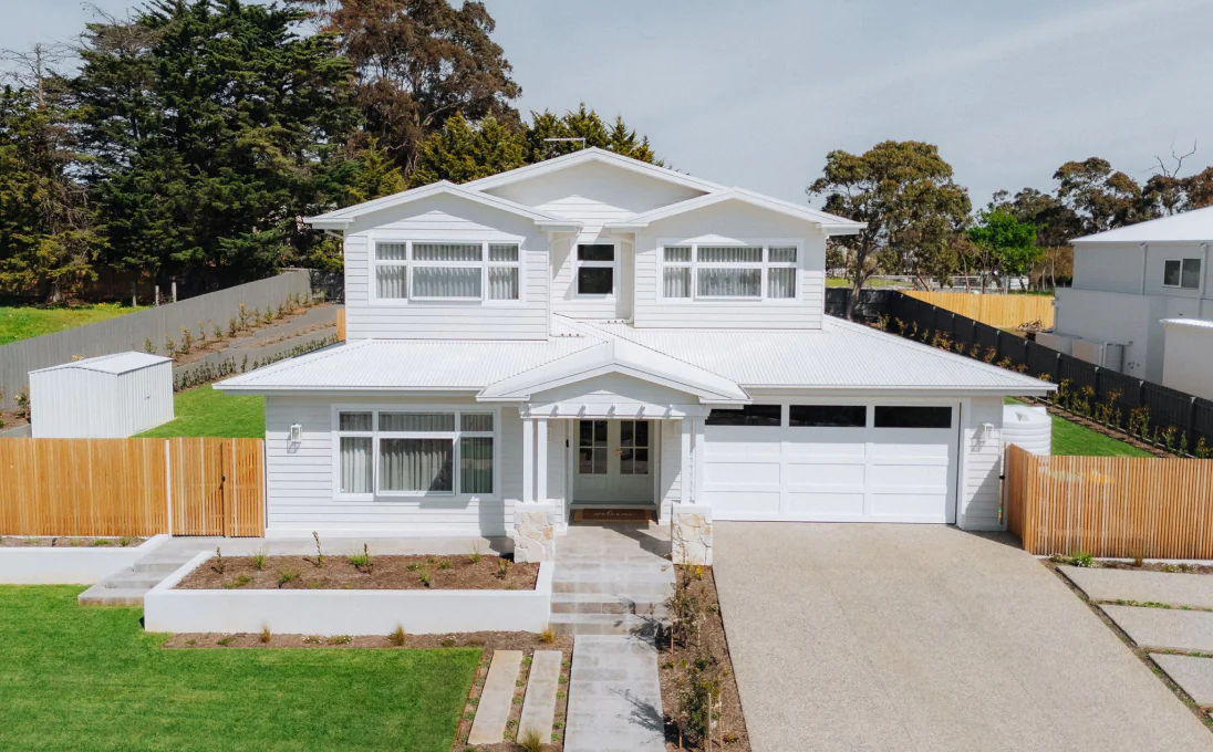 White two-story suburban house with a double garage, central front porch, and paved driveway