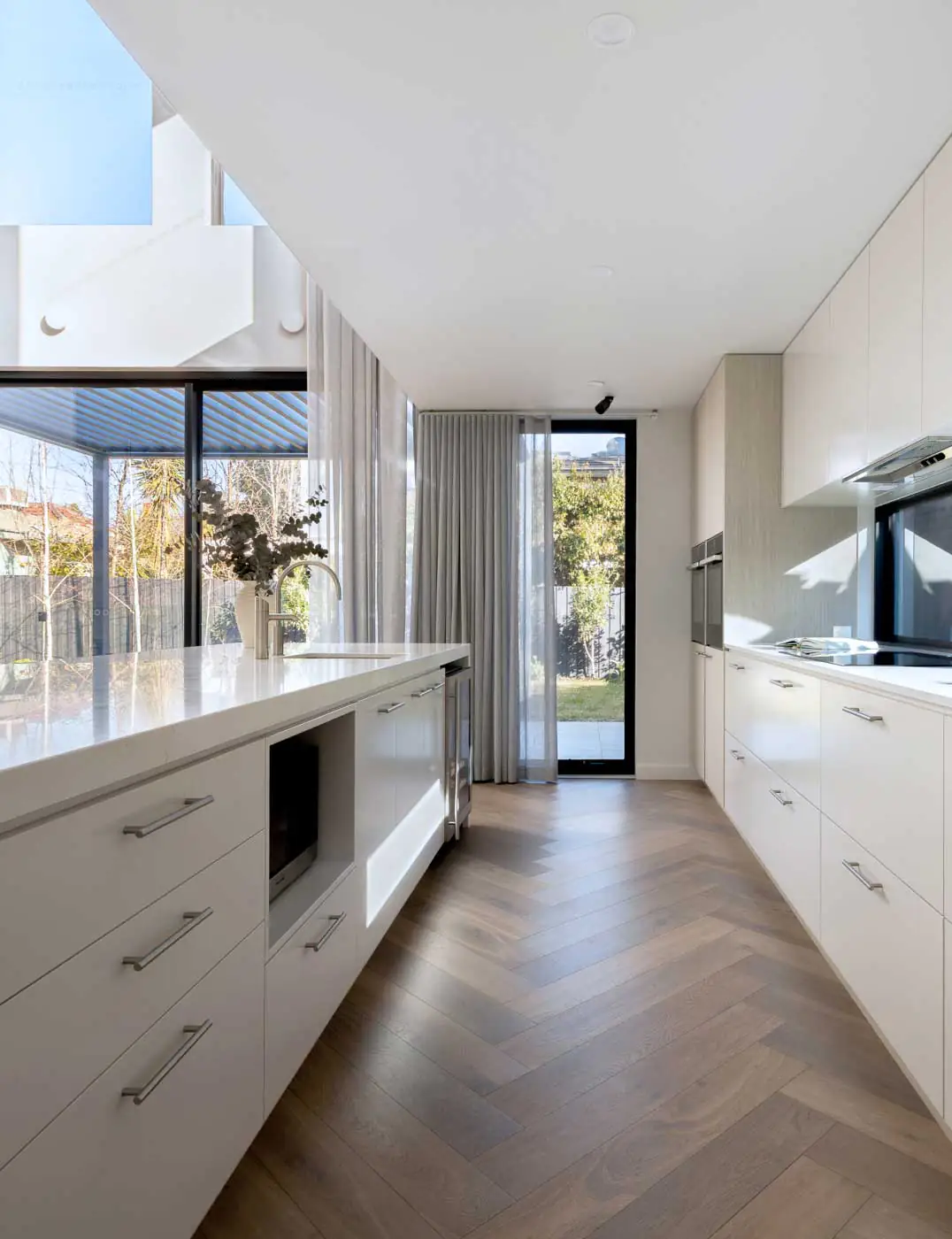 Bright modern kitchen with white cabinets, a long island, and a glass door opening to a sunny yard outside.