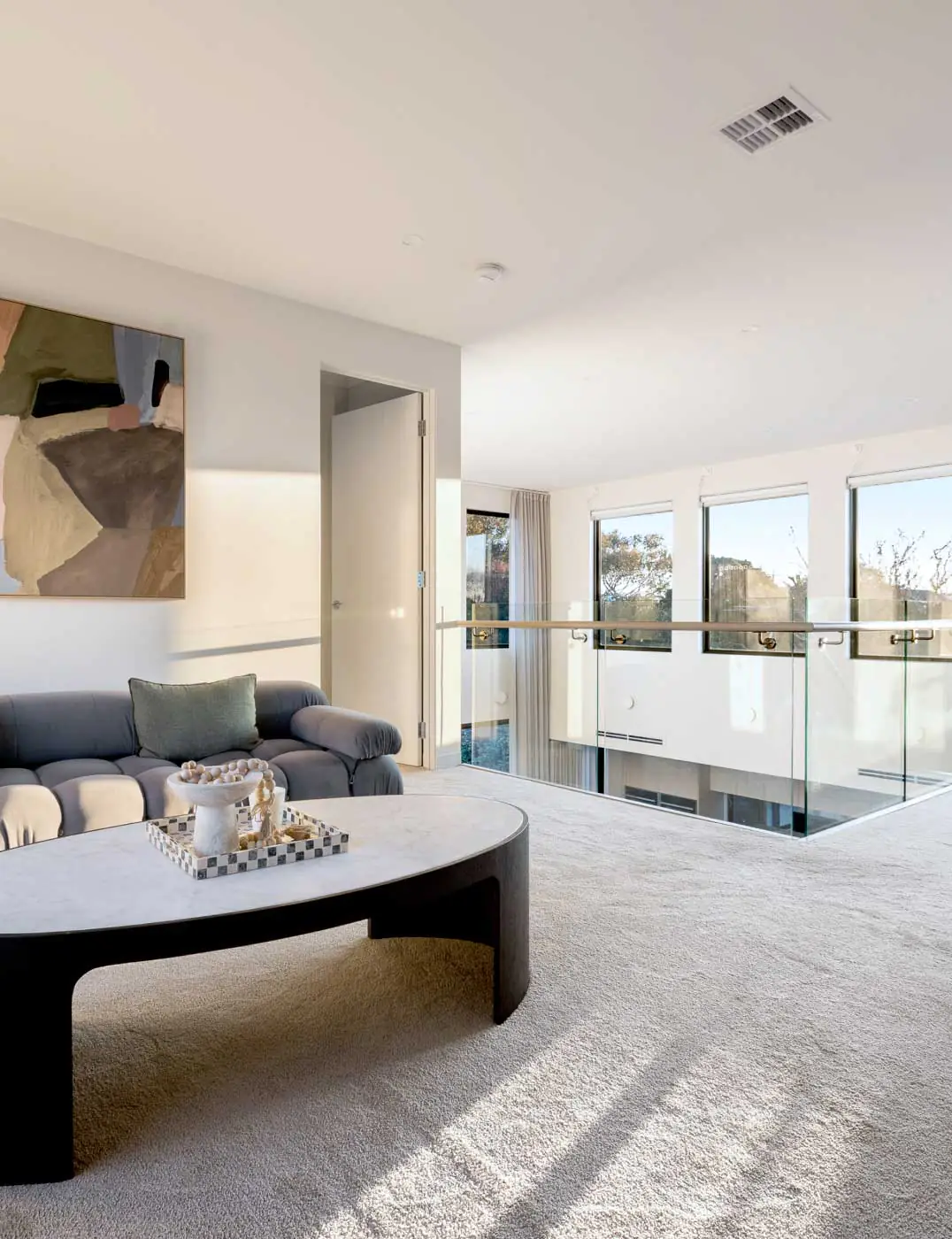 Sunlit modern living room with a gray sectional sofa, abstract wall art, and a white marble-topped coffee table.