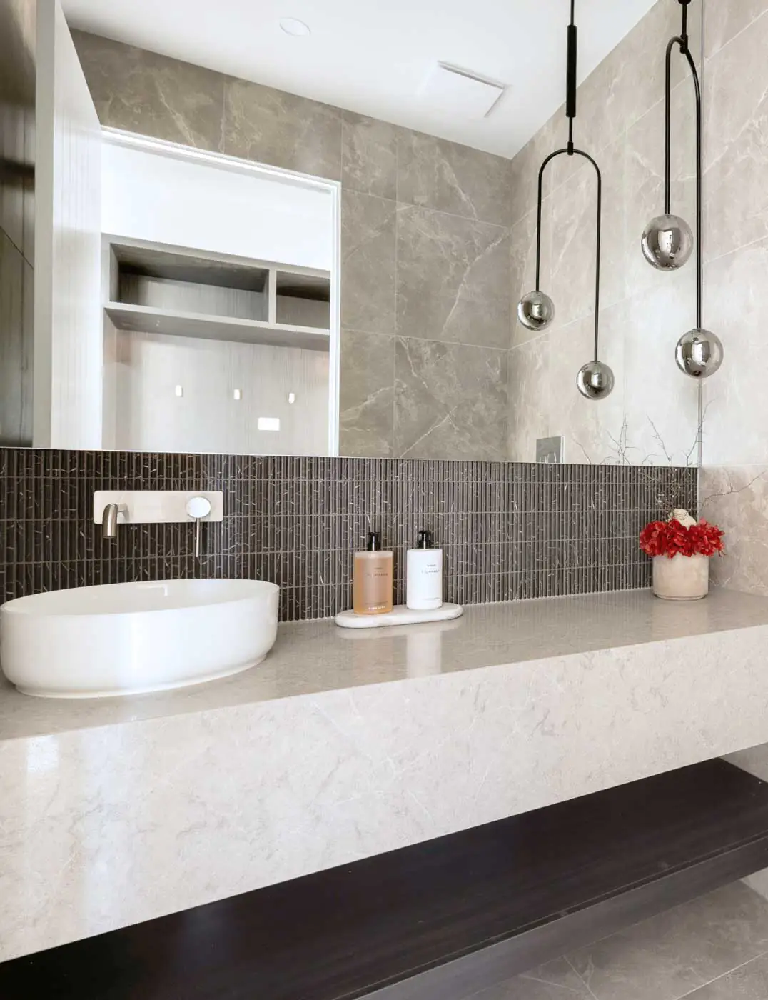 Modern bathroom vanity with a white vessel sink, dark small-tile backsplash, and hanging spherical pendant lights.